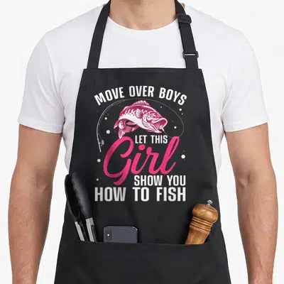 Cute fishing fisherman apron - Pink and white bass graphic with text Move Over Boys Let This Girl Show You How To Fish — shown on a black cotton canvas apron against a white background