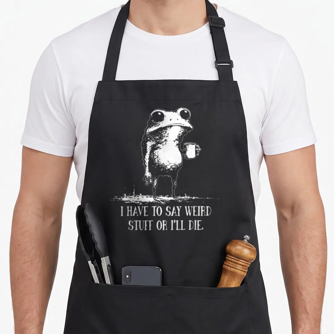 Ill meme apron - White line-art frog holding a mug with text I HAVE TO SAY WEIRD STUFF OR I'll DIE below — shown on a black cotton canvas apron against a white background