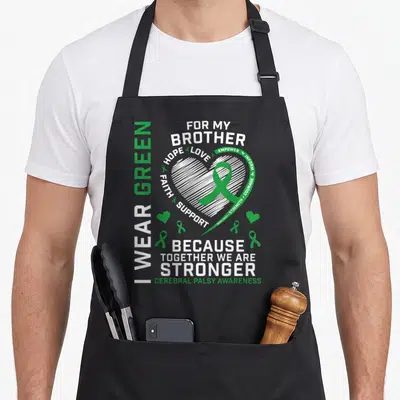 Brother cerebral palsy awareness apron - White sketched heart with green ribbon and vertical text reading I WEAR GREEN — shown on a black cotton canvas apron against a white background