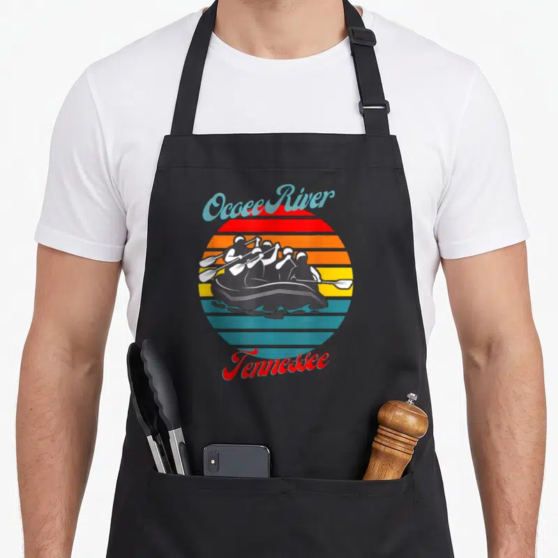 Ocoee canoeing apron - Retro sun graphic with rafters and Ocoee River Tennessee text in red orange yellow blue grey — shown on a black cotton canvas apron against a white background