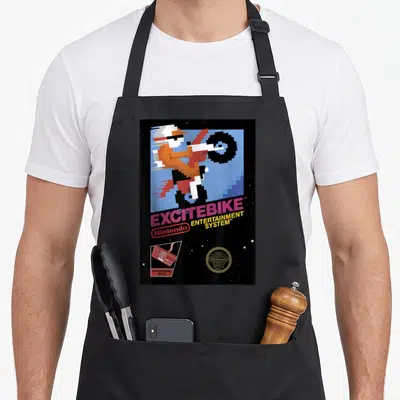 Funny excitebike game aprons - Pixelated motorcyclist doing a wheelie with Excitebike title and Nintendo seal on black — shown on a black cotton canvas apron against a white background