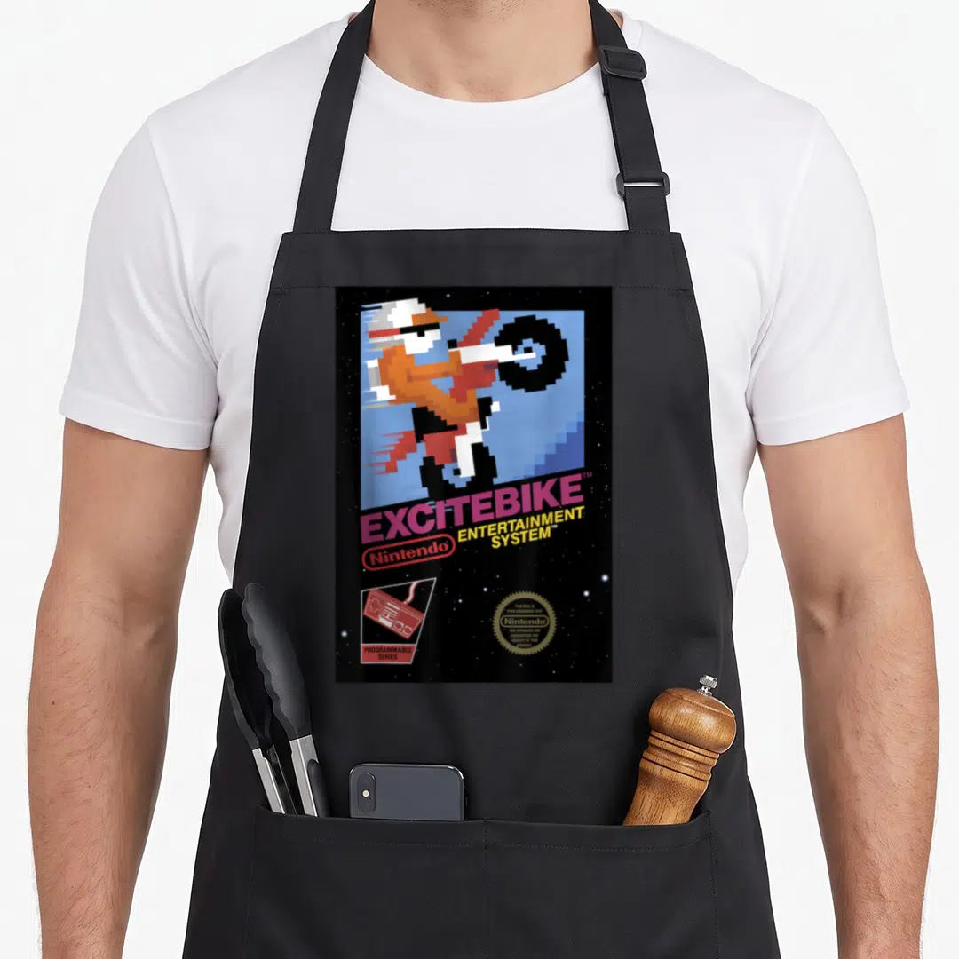 Funny excitebike game aprons - Pixelated motorcyclist doing a wheelie with Excitebike title and Nintendo seal on black — shown on a black cotton canvas apron against a white background