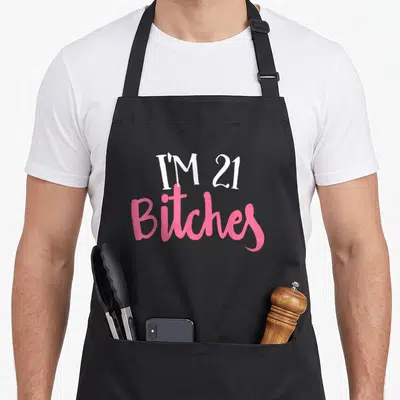 21st birthday party apron - Stacked white and pink text reading I'M 21 Bitches — shown on a black cotton canvas apron against a white background