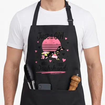 Breed dachshund apron - Floral dachshund silhouette in front of pink striped sun with hearts — shown on a black cotton canvas apron against a white background