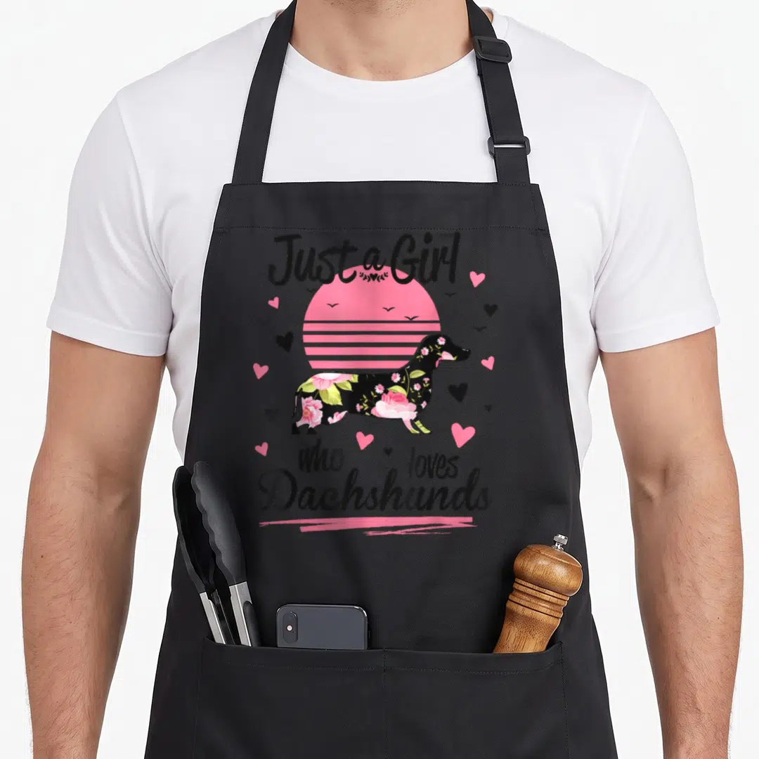 Breed dachshund apron - Floral dachshund silhouette in front of pink striped sun with hearts — shown on a black cotton canvas apron against a white background