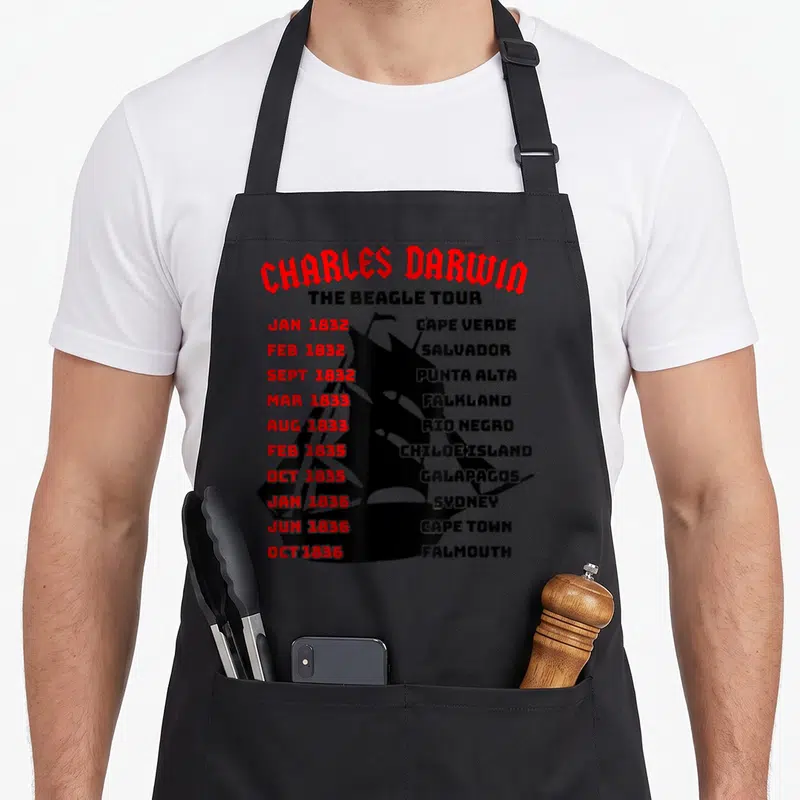 Naturalist science apron - Black ship silhouette with red dates and black location names for Darwin's Beagle Tour — shown on a black cotton canvas apron against a white background