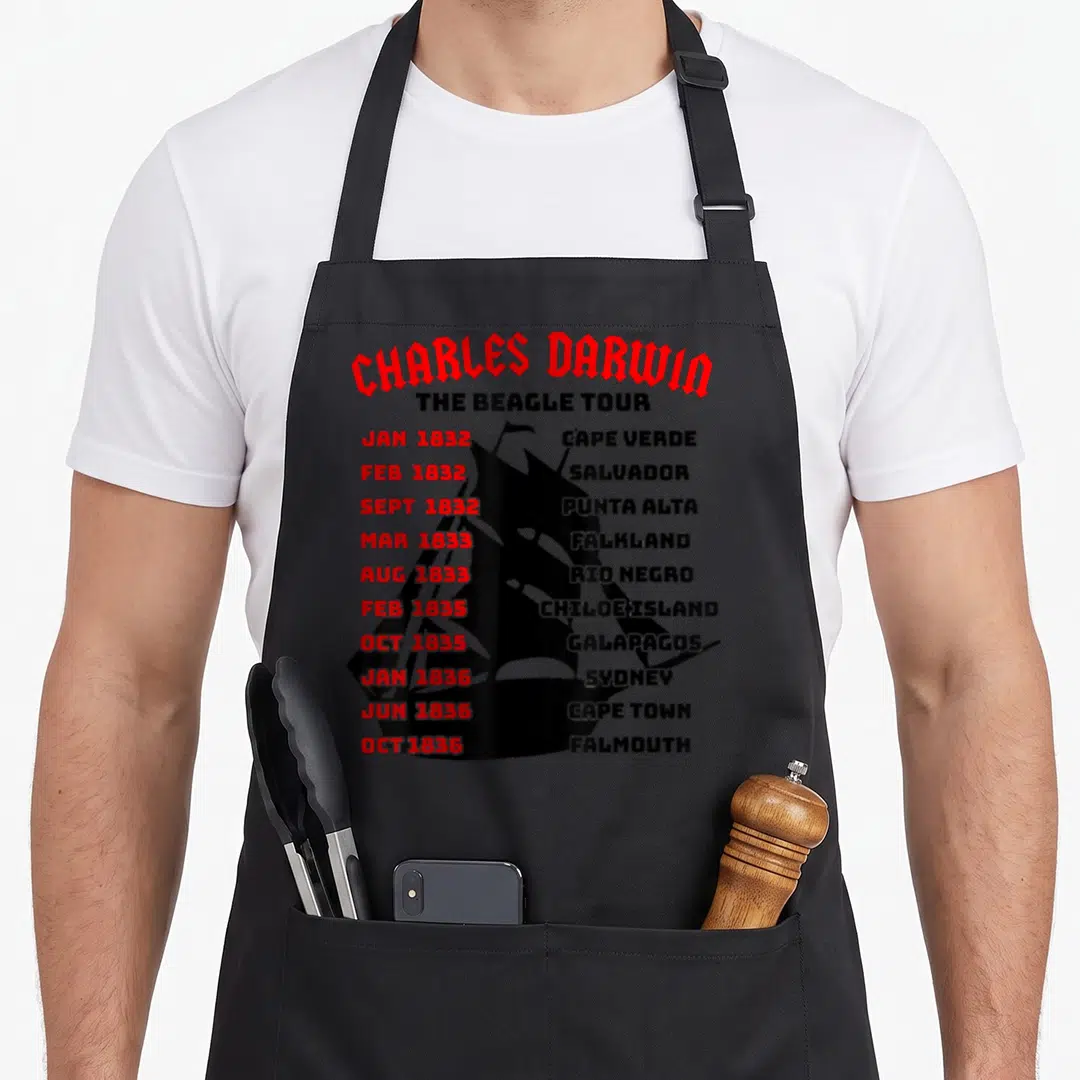 Naturalist science apron - Black ship silhouette with red dates and black location names for Darwin's Beagle Tour — shown on a black cotton canvas apron against a white background