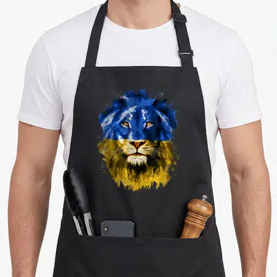 Ukraine face apron - Realistic lion head in blue and yellow splatter art with black details — shown on a black cotton canvas apron against a white background