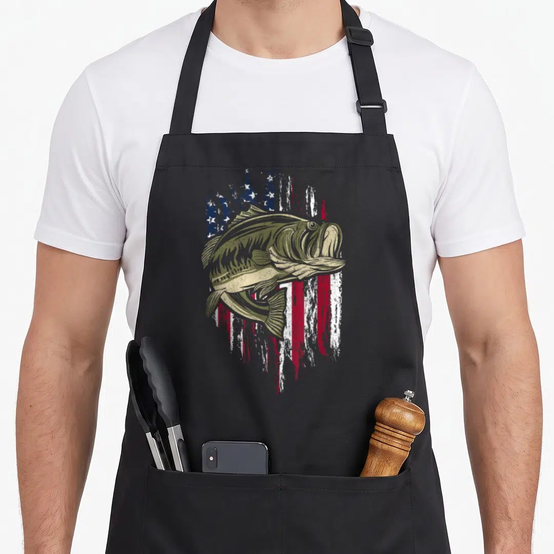 Bass 4th of july apron - Olive green bass fish over distressed red white and blue American flag graphic — shown on a black cotton canvas apron against a white background