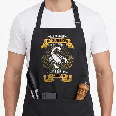 Sign scorpio birthday apron - White scorpion on gold zodiac wheel with banner text about women being born as Scorpio — shown on a black cotton canvas apron against a white background