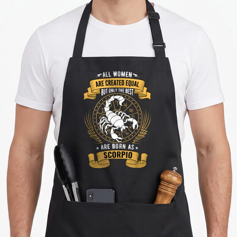 Sign scorpio birthday apron - White scorpion on gold zodiac wheel with banner text about women being born as Scorpio — shown on a black cotton canvas apron against a white background