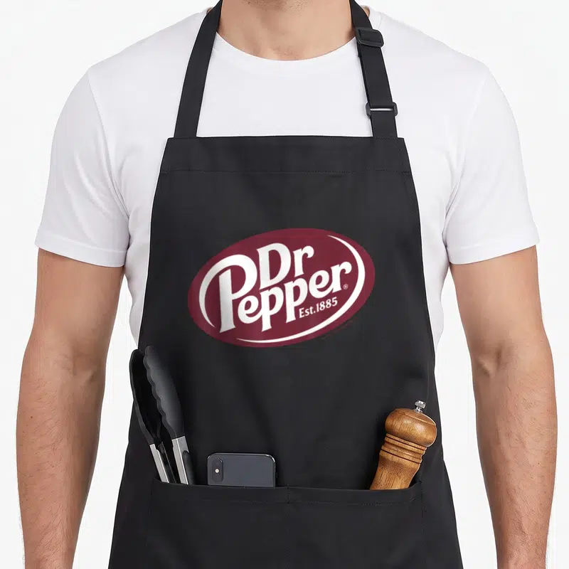 Pepper dr apron - Maroon oval with white Dr Pepper Est 1885 typography logo — shown on a black cotton canvas apron against a white background