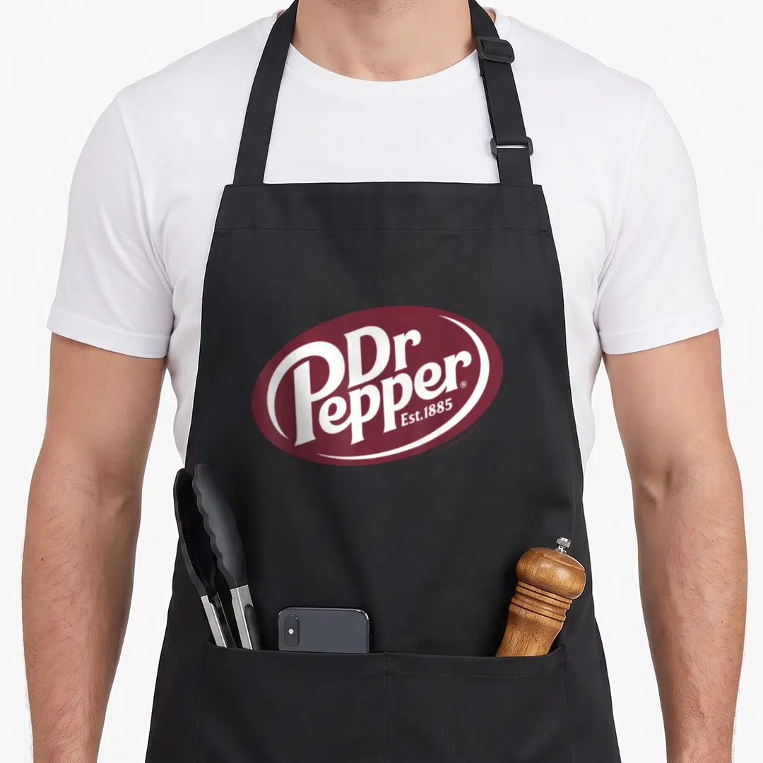 Pepper dr apron - Maroon oval with white Dr Pepper Est 1885 typography logo — shown on a black cotton canvas apron against a white background