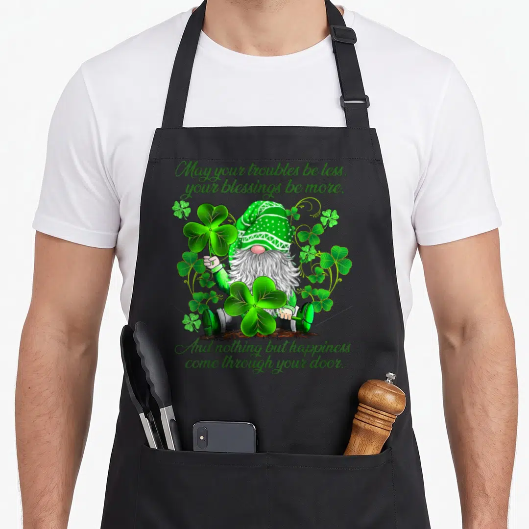 Christian st patrick day aprons - Cartoon gnome holding shamrocks with Irish blessing text in green script — shown on a black cotton canvas apron against a white background