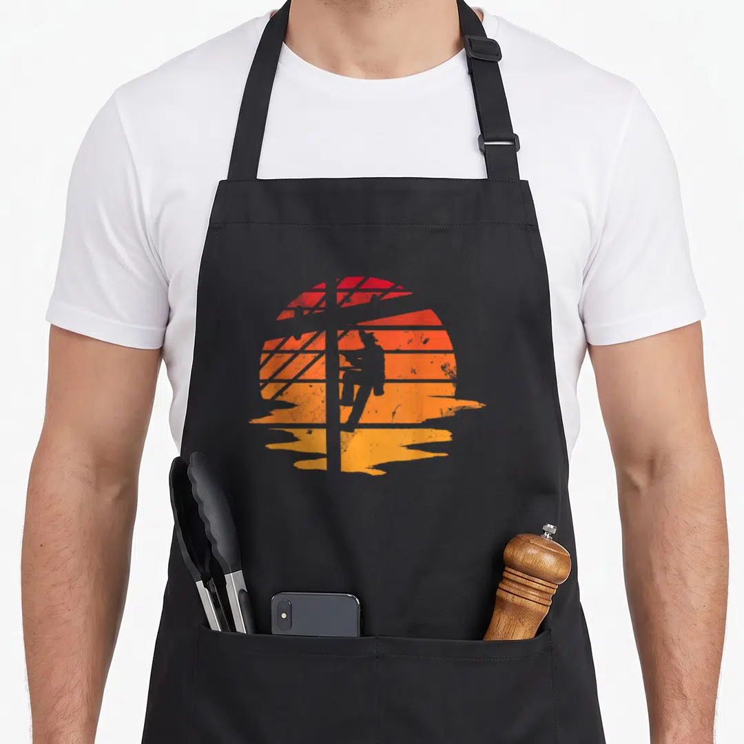 Distressed electrician apron - Grey lineman silhouette on red orange yellow distressed striped sunburst circle — shown on a black cotton canvas apron against a white background