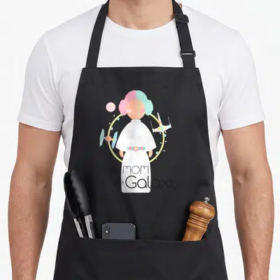 Funny galaxy princess apron - Minimalist woman in white dress flanked by spaceships with text Best mom in the Galaxy — shown on a black cotton canvas apron against a white background