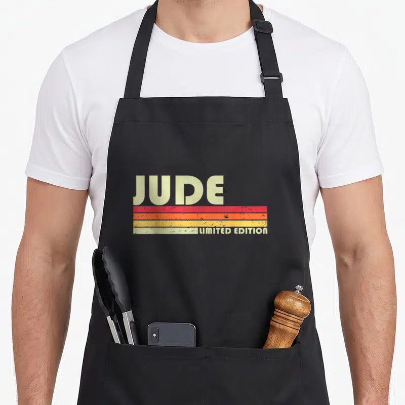 Husband vintage style christmas aprons - JUDE LIMITED EDITION text with red orange yellow stripes in retro font — shown on a black cotton canvas apron against a white background