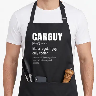 Car auto apron - White CARGUY dictionary definition text stacked on dark background with pocket details — shown on a black cotton canvas apron against a white background