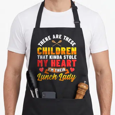 Teacher cafeteria aprons - Stacked text with crossed spoons, hearts, and orange ribbon reading There Are These Children — shown on a black cotton canvas apron against a white background