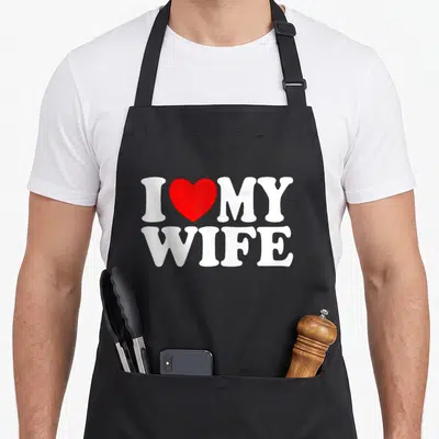 Funny wife husband apron - I MY WIFE white text with red heart symbol centered on front panel — shown on a black cotton canvas apron against a white background