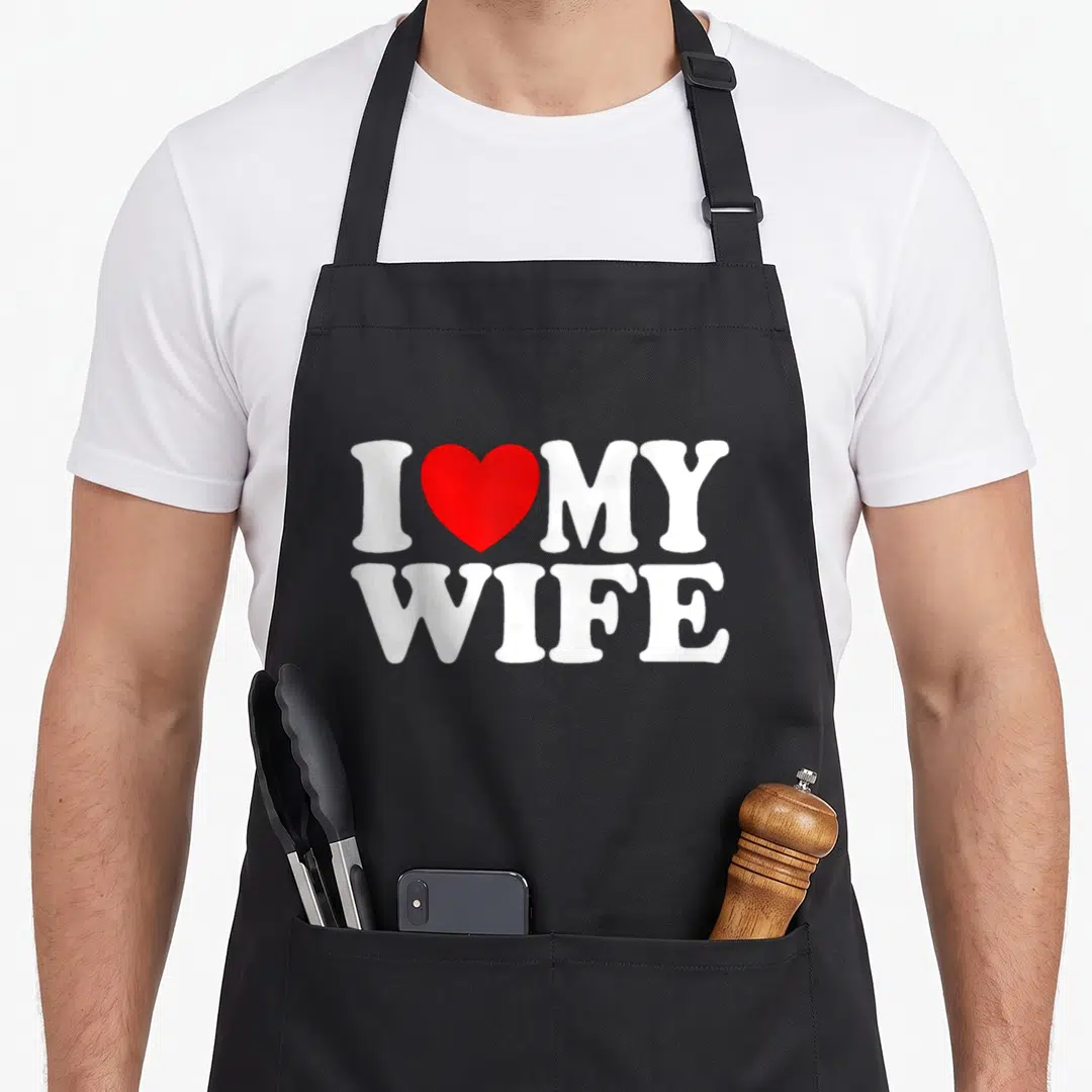 Funny wife husband apron - I MY WIFE white text with red heart symbol centered on front panel — shown on a black cotton canvas apron against a white background