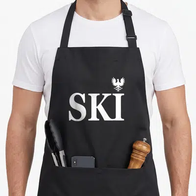 Heritage polish aprons - White SKI text with small eagle symbol above the letter I — shown on a black cotton canvas apron against a white background