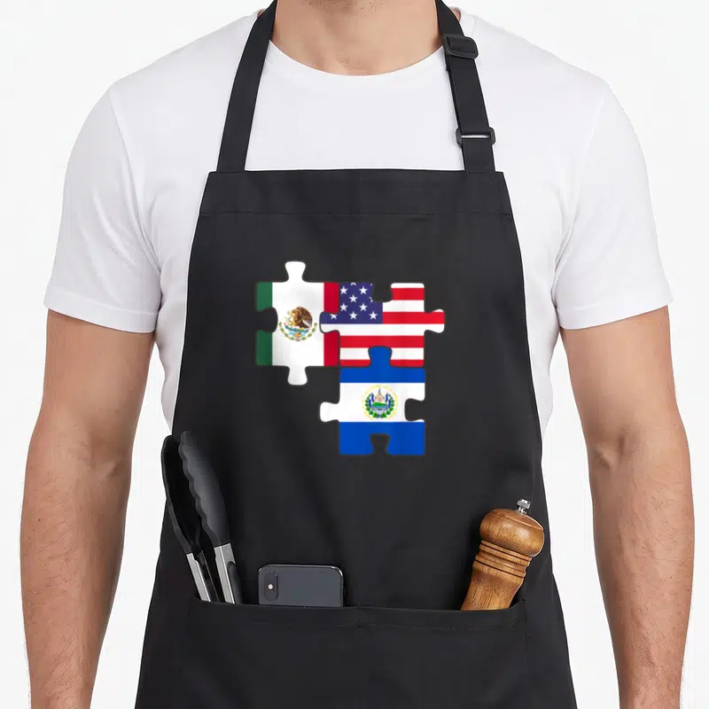 Mexican salvadoran apron - Three puzzle pieces displaying Mexican, US, and Salvadoran flags in red white blue and green — shown on a black cotton canvas apron against a white background