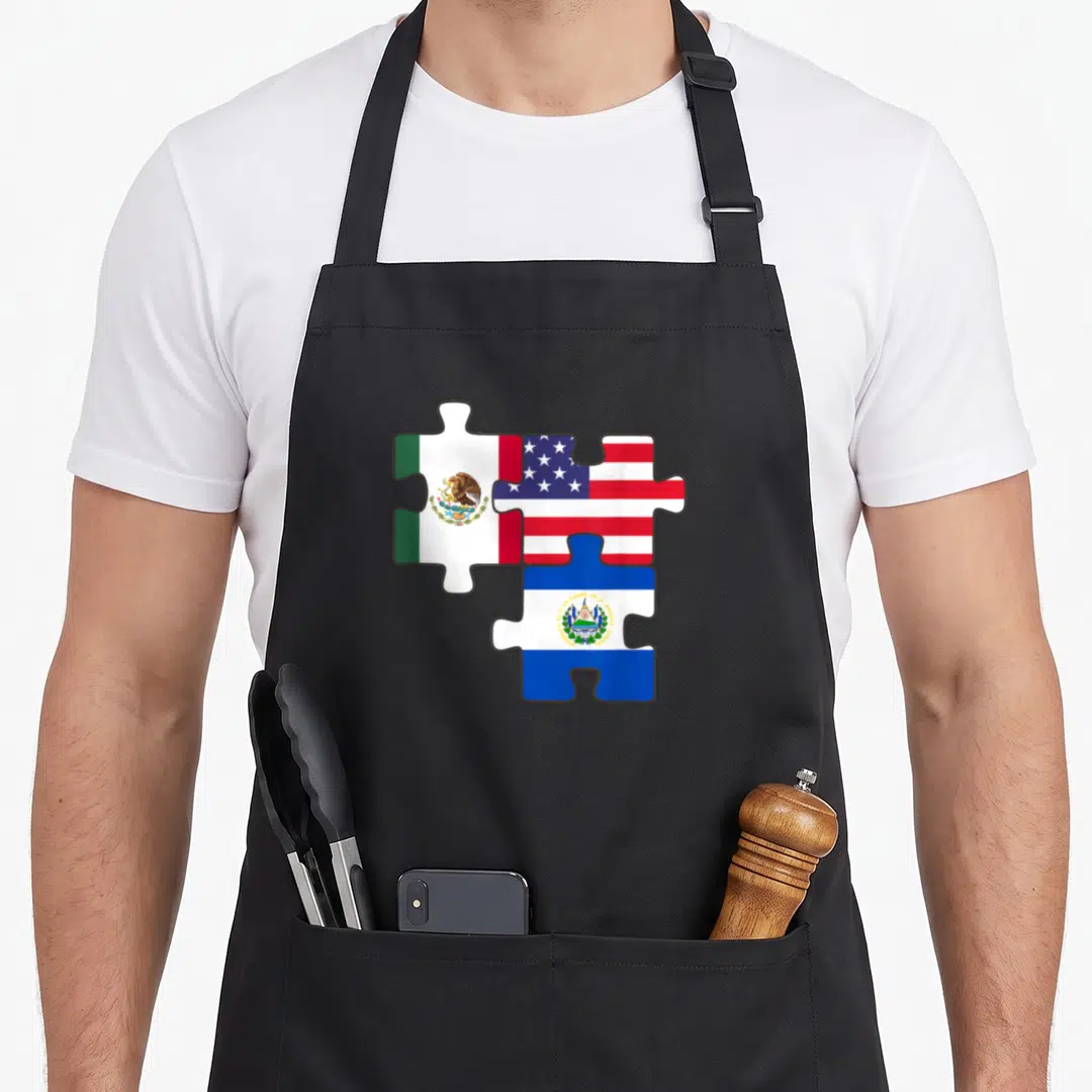 Mexican salvadoran apron - Three puzzle pieces displaying Mexican, US, and Salvadoran flags in red white blue and green — shown on a black cotton canvas apron against a white background