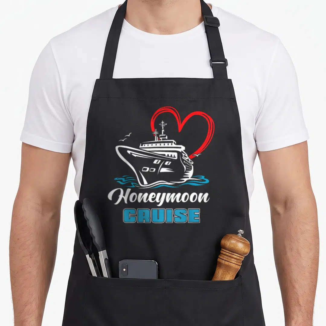 Honeymoon newlywed aprons - White cruise ship with red heart outline and blue Honeymoon CRUISE text — shown on a black cotton canvas apron against a white background