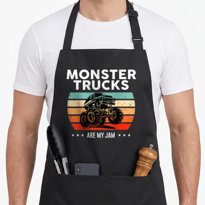 Jam truck aprons - Retro monster truck silhouette over teal orange and red stripes with white text and six stars — shown on a black cotton canvas apron against a white background