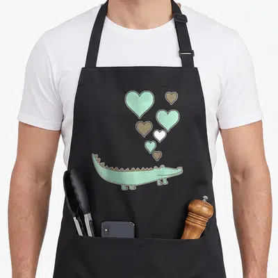 Vintage alligator apron - Cartoon mint crocodile with six floating hearts in mint, brown, and white — shown on a black cotton canvas apron against a white background