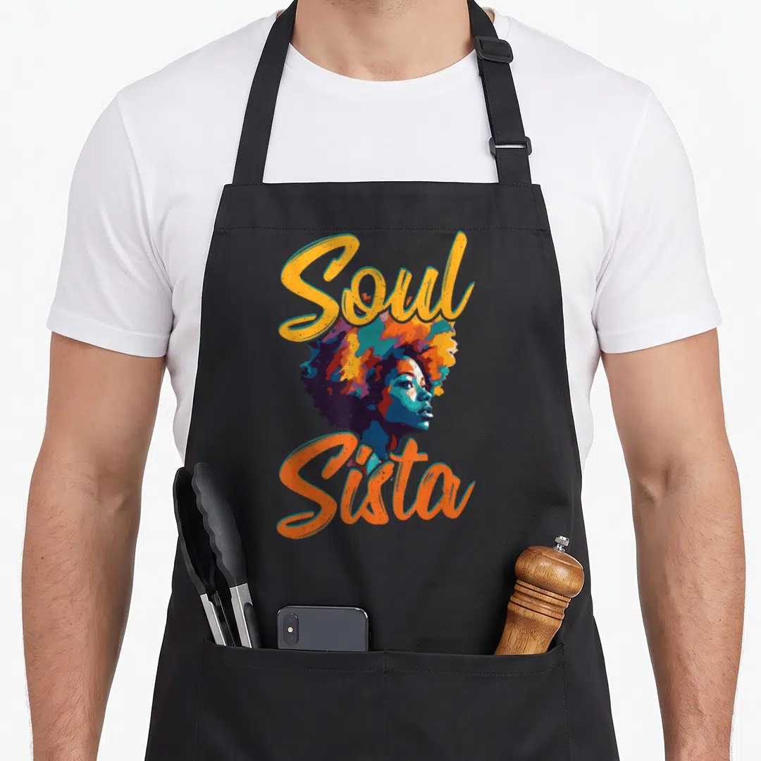 Cute funk 70s apron - Soul Sista text framing colorful cartoon woman profile with large afro in yellow orange blue — shown on a black cotton canvas apron against a white background