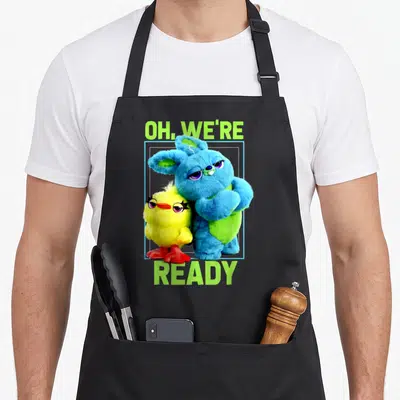 Ducky bunny apron - Blue bunny and yellow chick inside blue frame with OH WE'RE READY lime green text — shown on a black cotton canvas apron against a white background
