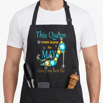 Living baking queen apron - Cyan and gold high heel shoe made of gems with stacked text This Queen was born in MAY — shown on a black cotton canvas apron against a white background