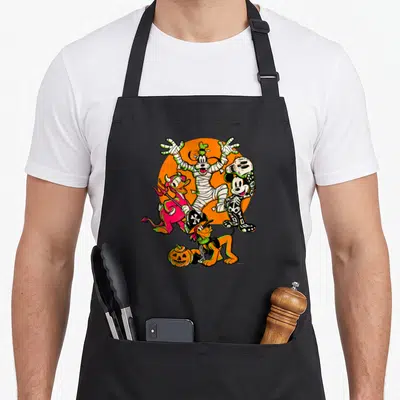 Donald halloween white apron - Goofy mummy Donald devil Mickey skeleton Pluto pirate orange circle — shown on a black cotton canvas apron against a white background