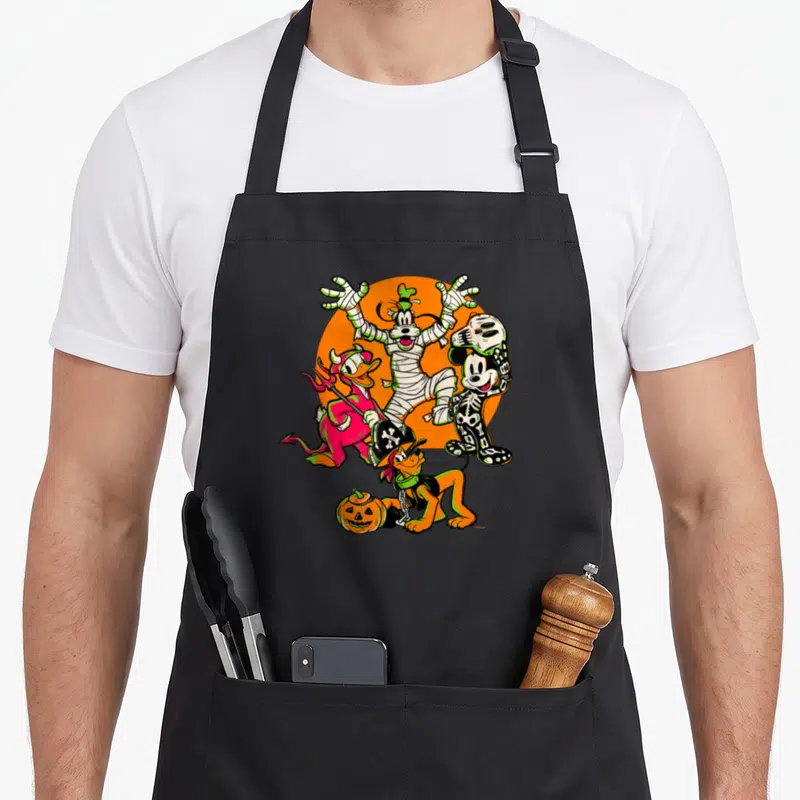 Donald halloween white apron - Goofy mummy Donald devil Mickey skeleton Pluto pirate orange circle — shown on a black cotton canvas apron against a white background