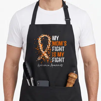 Fight leukemia awareness apron - Distressed heart ribbon in orange white peach next to stacked text My Mom's Fight Is — shown on a black cotton canvas apron against a white background