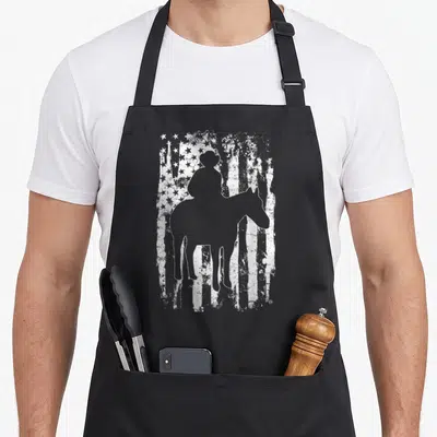 Funny rodeo cowboy apron - Grey cowboy on horseback silhouette over distressed white stars and stripes — shown on a black cotton canvas apron against a white background
