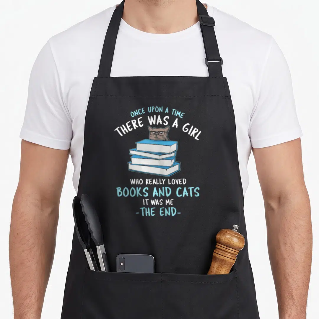 Cat once upon an apron - Cartoon cat head from behind stack of three blue and white books with story text — shown on a black cotton canvas apron against a white background
