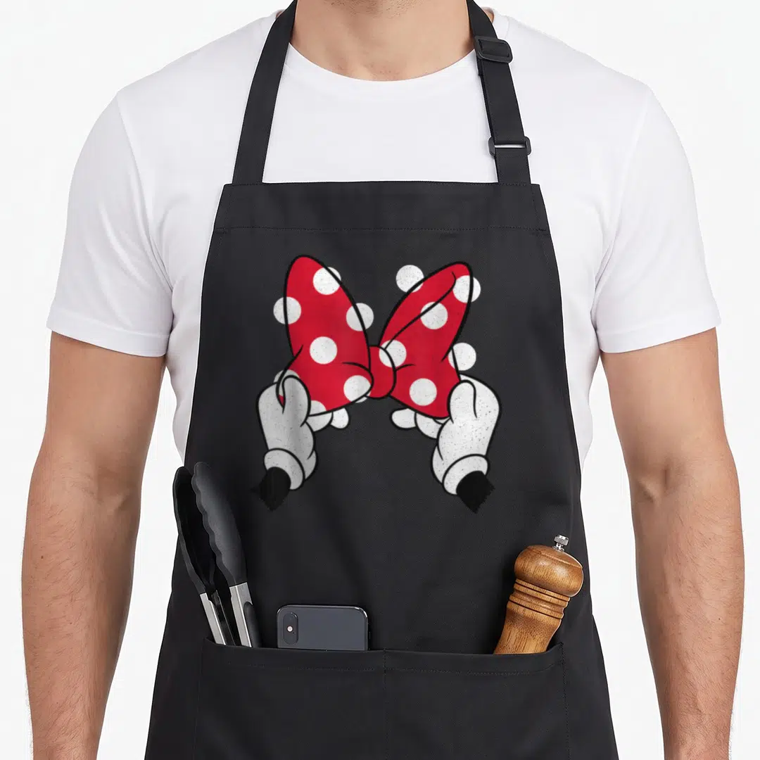 Mouse bow apron - Red polka dot bow held by two white gloved cartoon hands — shown on a black cotton canvas apron against a white background