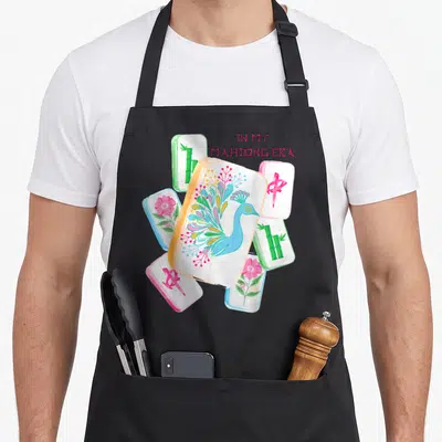 Era mahjong apron - Cartoon peacock and bamboo mahjong tiles with pink text IN MY MAHJONG ERA — shown on a black cotton canvas apron against a white background