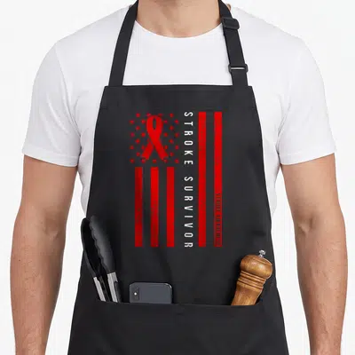 Month stroke awareness apron - Red ribbon and stars with vertical STROKE SURVIVOR text on distressed background — shown on a black cotton canvas apron against a white background