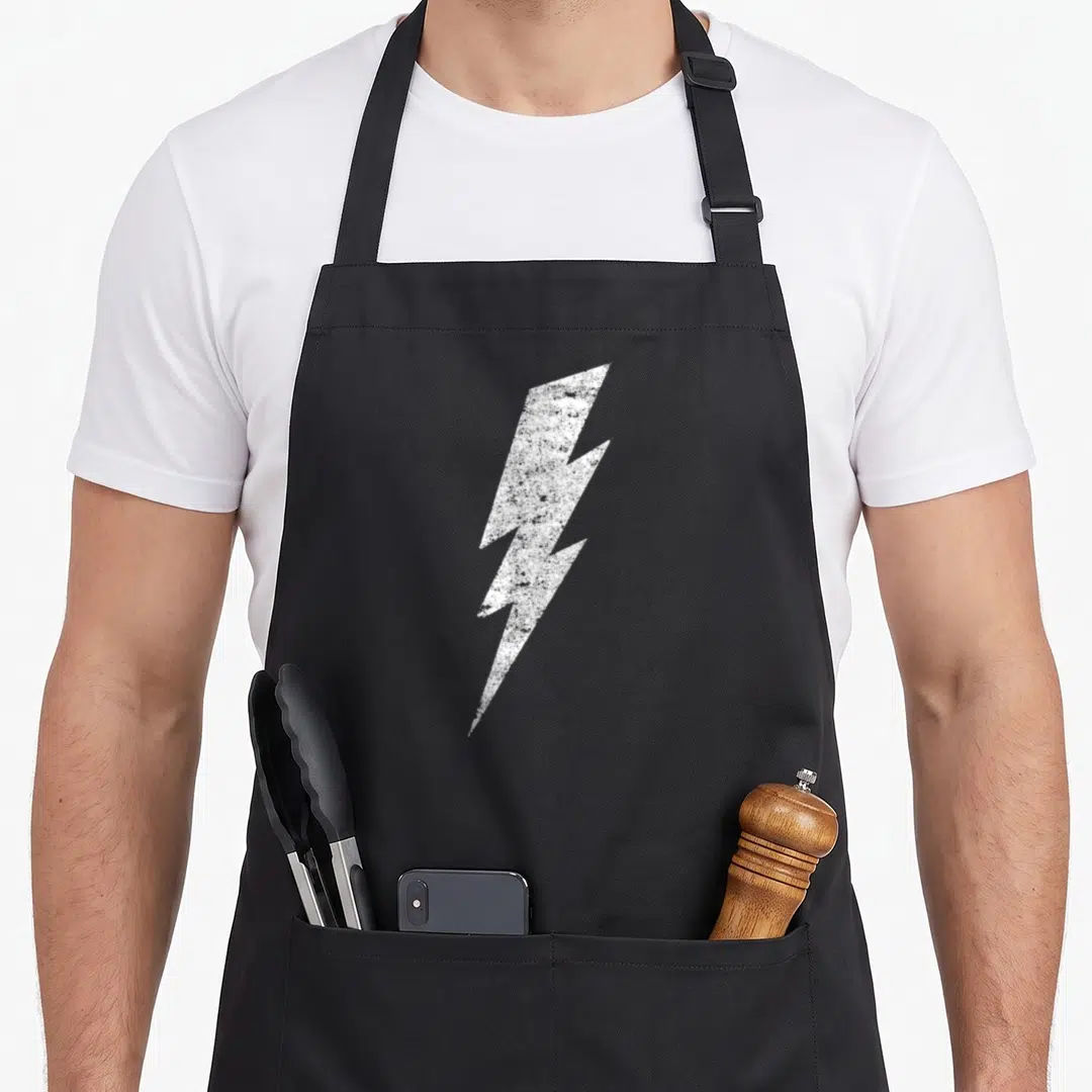 Bold distressed apron - White distressed lightning bolt graphic centered on black fabric — shown on a black cotton canvas apron against a white background