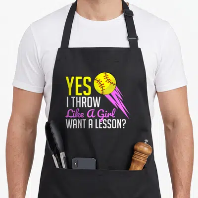 Softball player game aprons - Yes I Throw Like A Girl text with yellow softball and pink motion lines — shown on a black cotton canvas apron against a white background