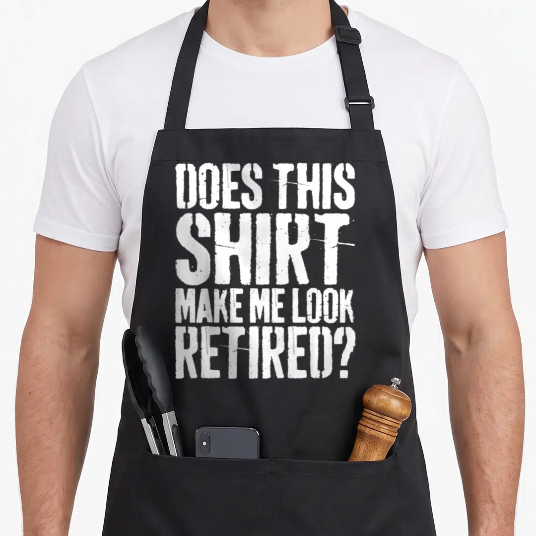Funny doe retirement apron - White stacked text DOES THIS SHIRT MAKE ME LOOK RETIRED on black background — shown on a black cotton canvas apron against a white background