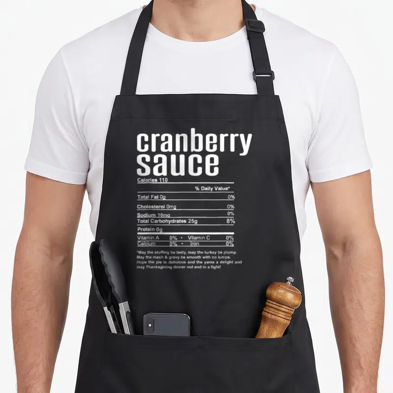 Thanksgiving christmas apron - White nutrition facts label for cranberry sauce with sarcastic holiday wishes printed — shown on a black cotton canvas apron against a white background