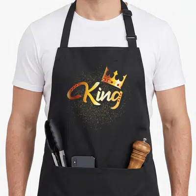 Funny king couple apron - Gold King text with red gems and scattered glitter under a crown — shown on a black cotton canvas apron against a white background