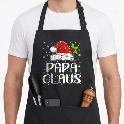 Papa christmas lights apron - Red Santa hat wrapped in multicolored lights above PAPA CLAUS text with holly — shown on a black cotton canvas apron against a white background