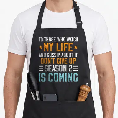 Those gossip apron - Stacked white orange and blue distressed text reading To Those Who Watch My Life And Gossip About — shown on a black cotton canvas apron against a white background