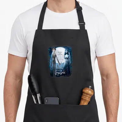 Poster bride apron - Two gothic characters holding hands under a moon with text There's been a grave misunderstanding — shown on a black cotton canvas apron against a white background